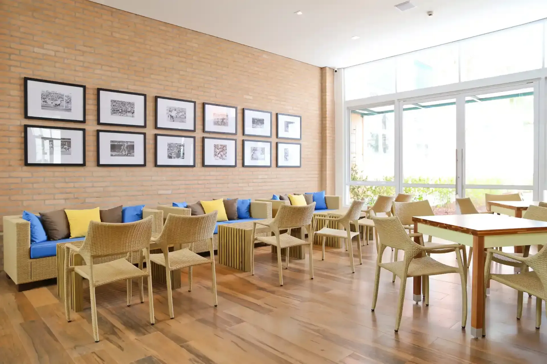 Um café bem iluminado com parede de tijolos, obras de arte, mesas e cadeiras e grandes janelas.