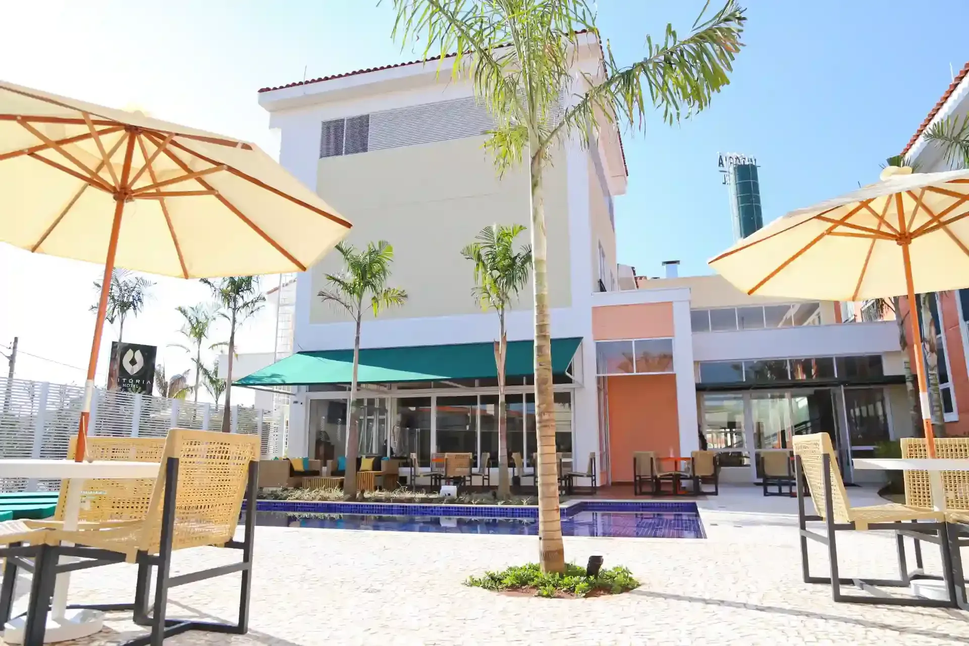 Café ao ar livre com mesas, guarda-sóis e prédio ao fundo em um dia ensolarado.