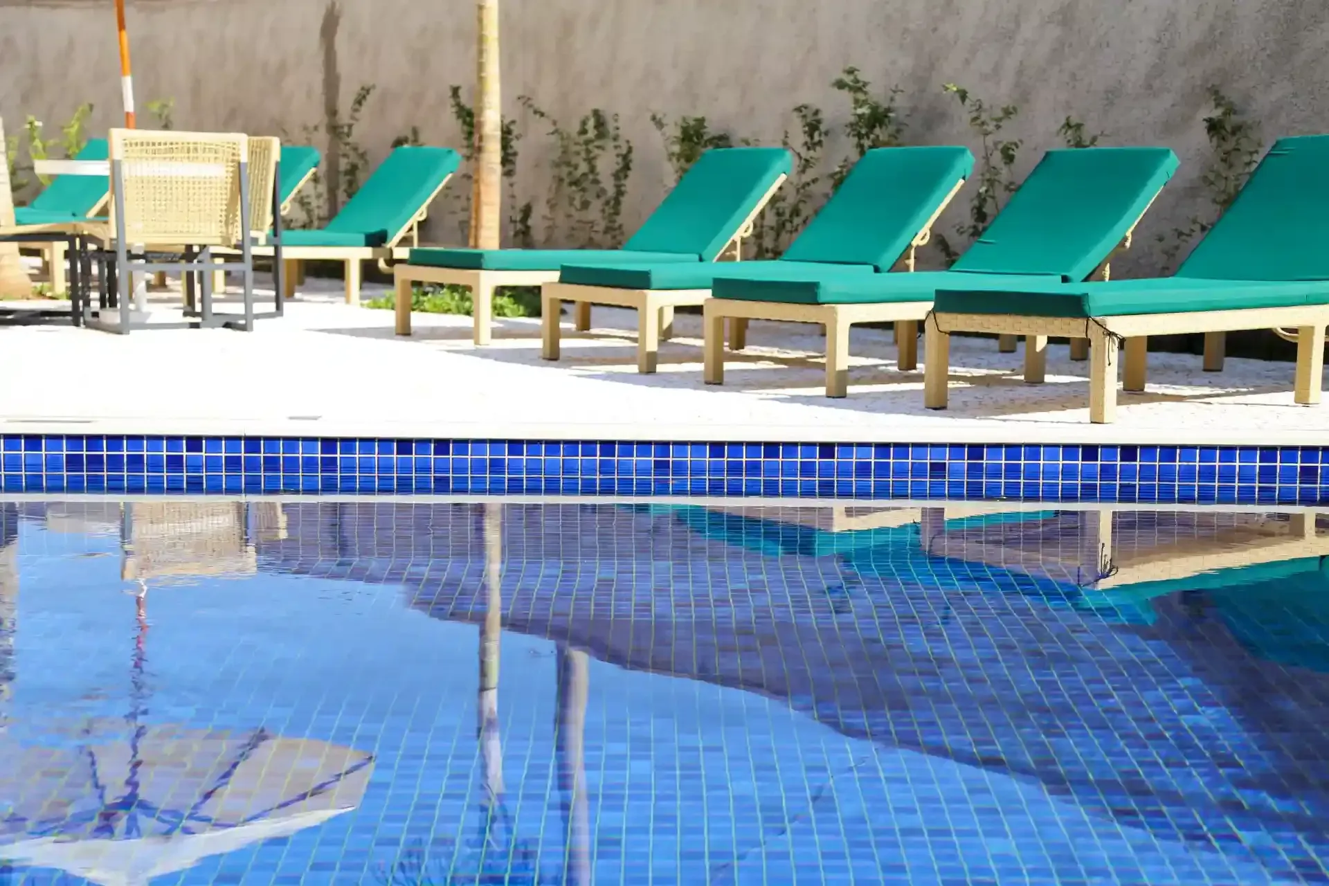 Piscina com espreguiçadeiras turquesa, refletindo um céu ensolarado.