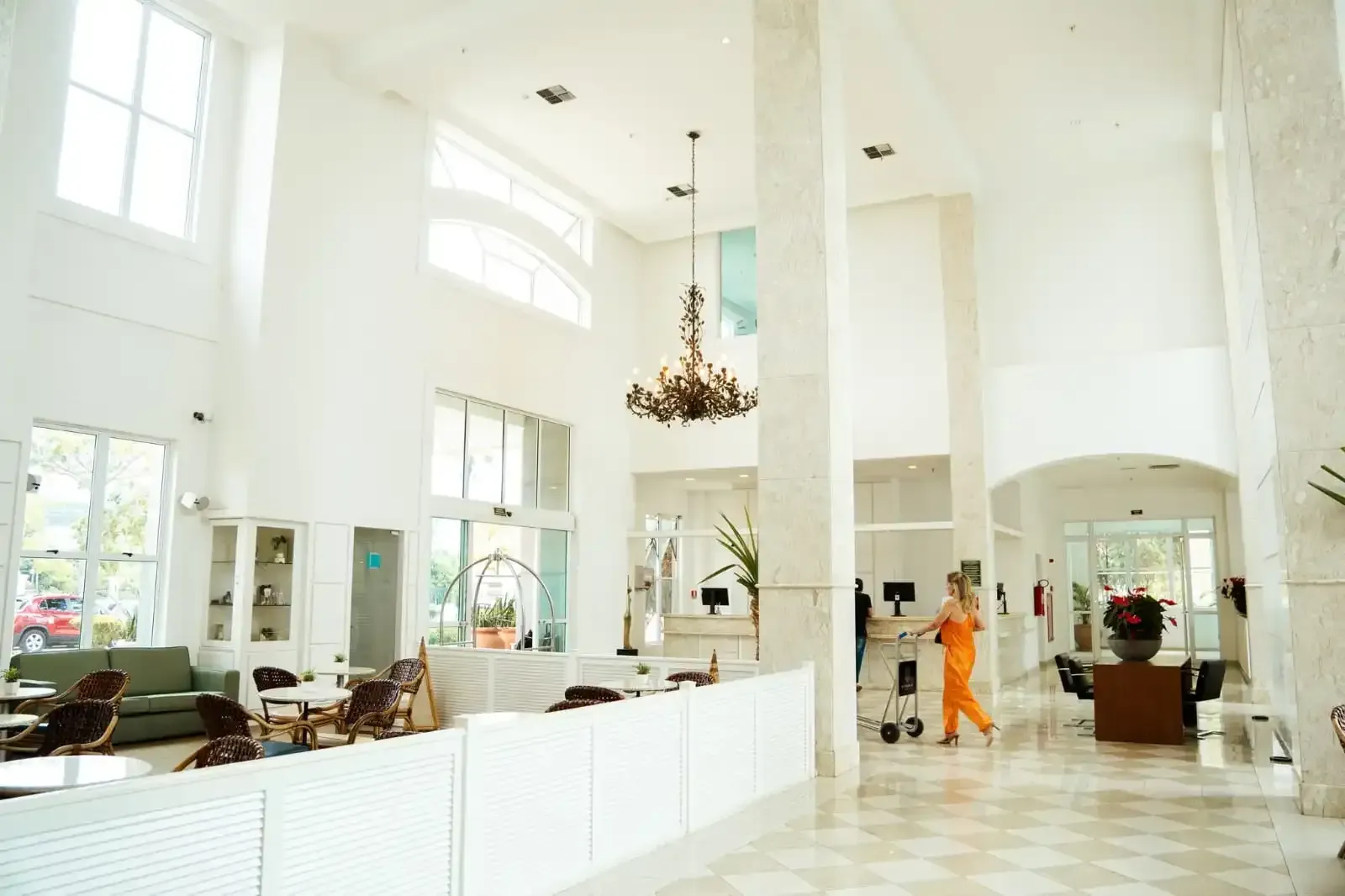 Hall de entrada amplo e luminoso, todo branco, com pé-direito alto, janelas grandes, lustre e uma pessoa caminhando.