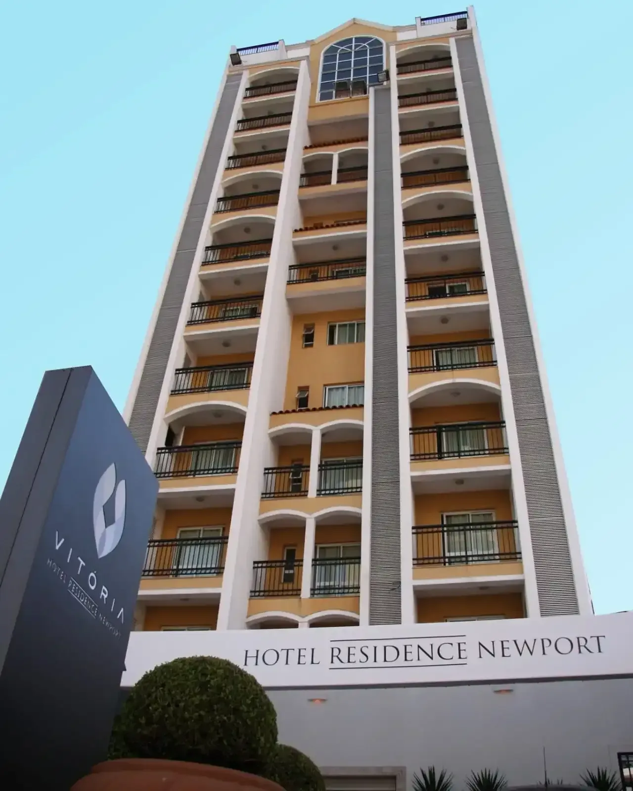 Hotel Residence Newport, prédio alto amarelo e branco com varandas; placa na frente.