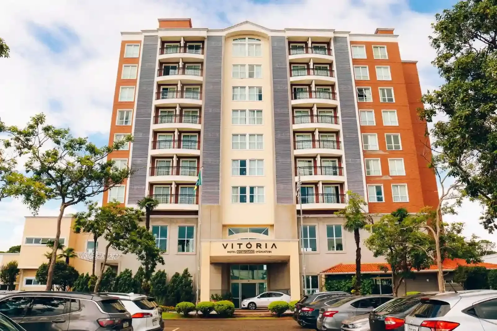 Fachada do Hotel Vitória, edifício de vários andares com varandas, exterior em tons de bege e tijolo, carros estacionados em frente.