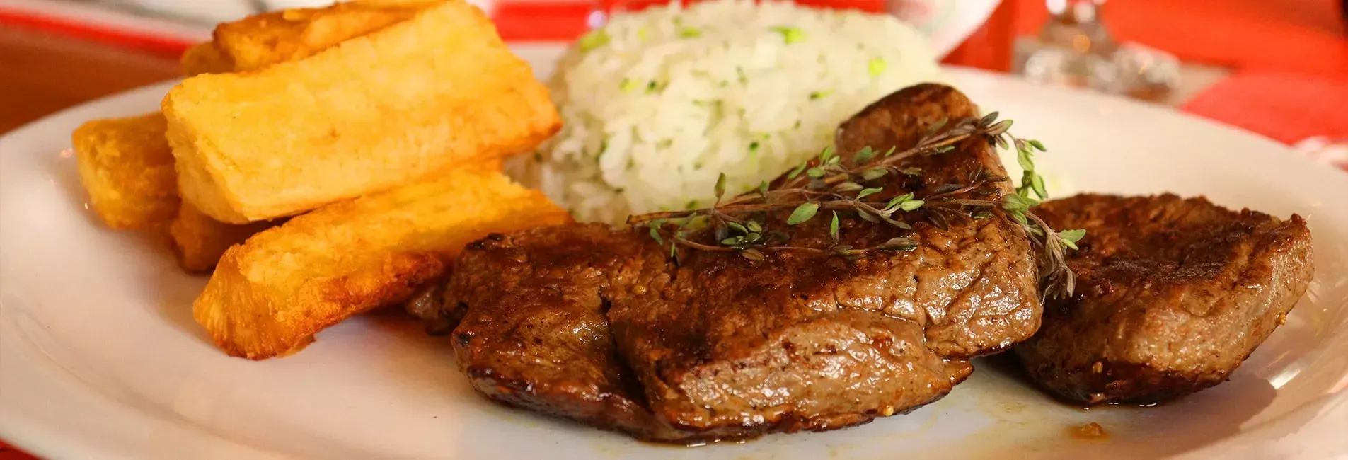 Bife, arroz e palitos de batata fritos num prato branco.