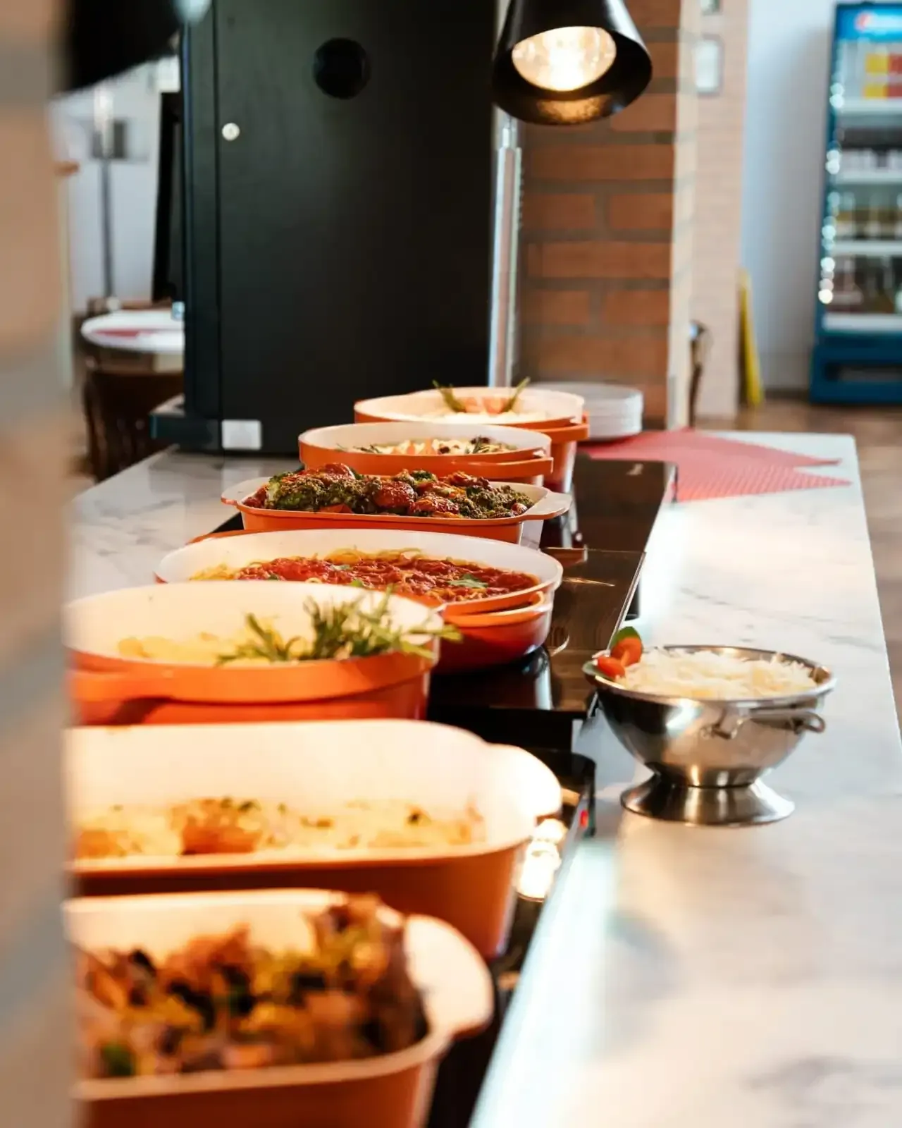 Buffet com diversos pratos em recipientes de cerâmica laranja e uma tigela de prata.