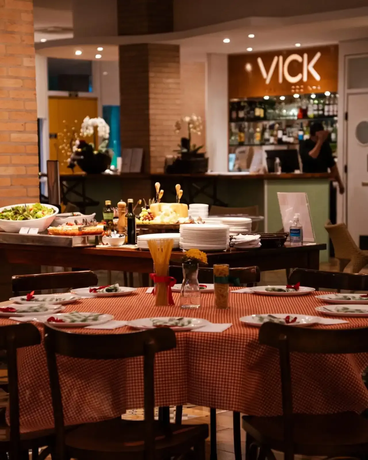 Área de jantar do restaurante com mesas redondas preparadas para as refeições, um buffet e um bar ao fundo.