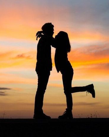 Uma silhueta de um homem e uma mulher se beijando ao pôr do sol.
