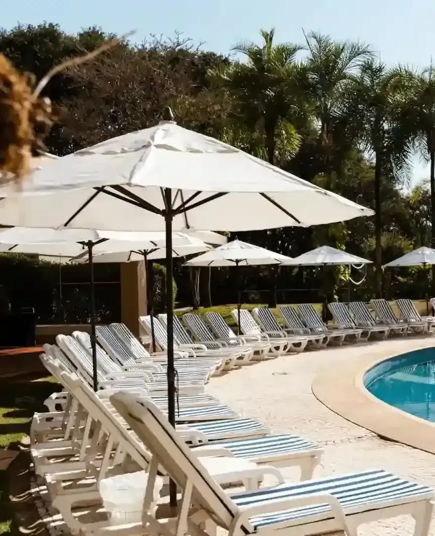 Cena à beira da piscina com guarda-sóis brancos, espreguiçadeiras listradas e uma piscina azul.