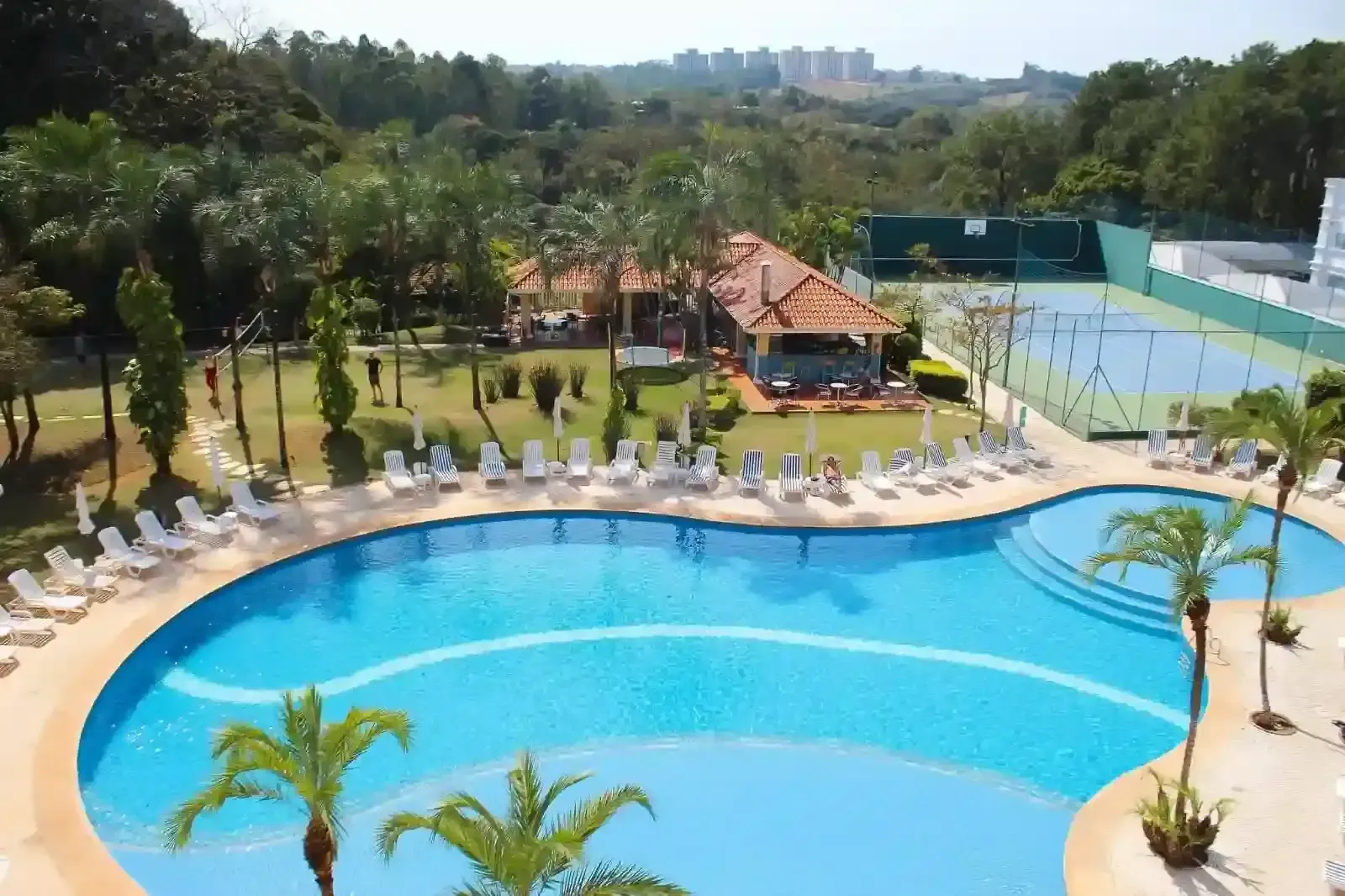 Piscina e área de lazer com espreguiçadeiras, quadra de tênis e restaurante.
