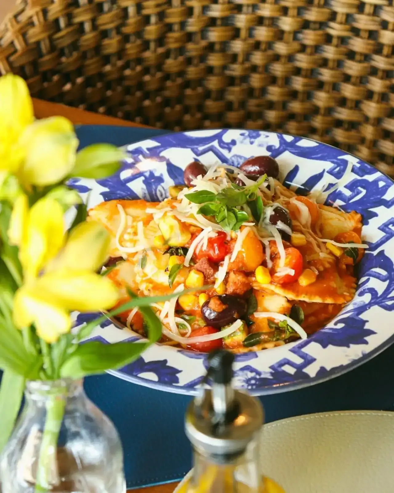 Enchiladas com legumes e queijo em um prato com estampa azul e branca, com flores em primeiro plano.