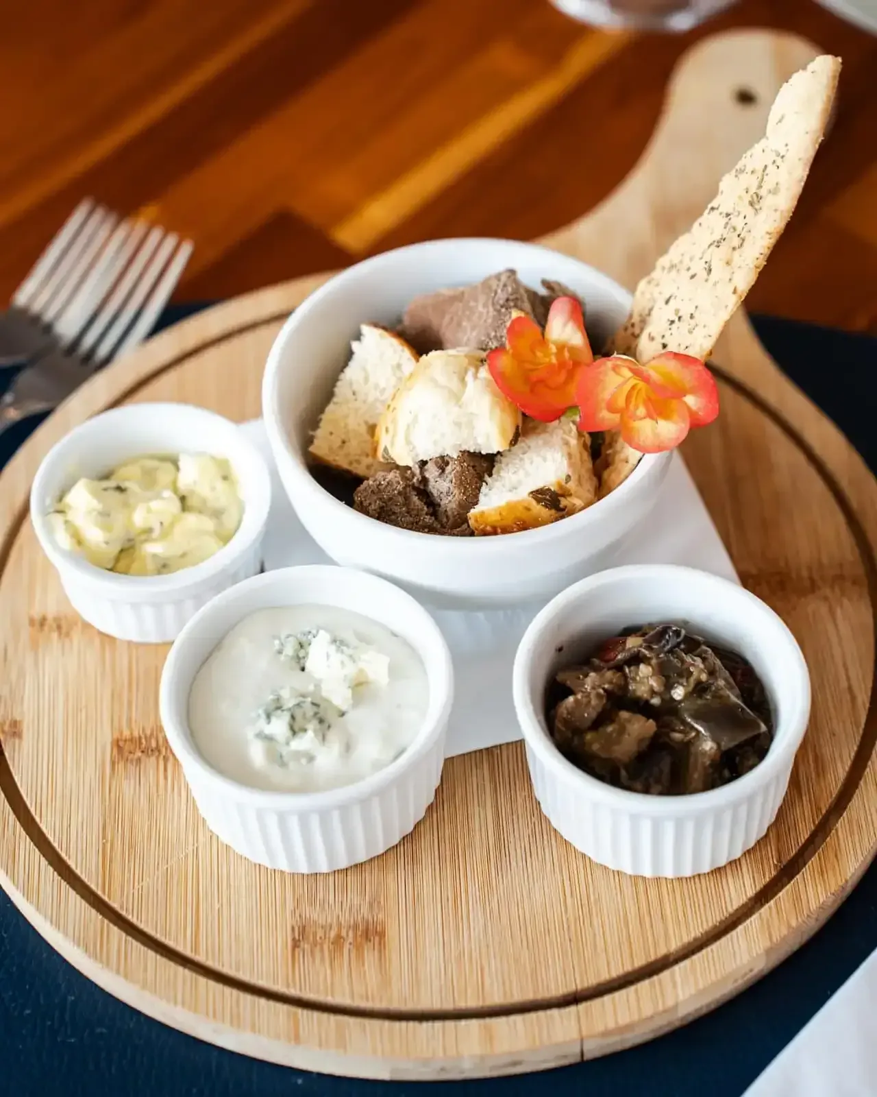 Tábua de madeira com pão e três molhos para mergulhar: manteiga, queijo azul e berinjela.