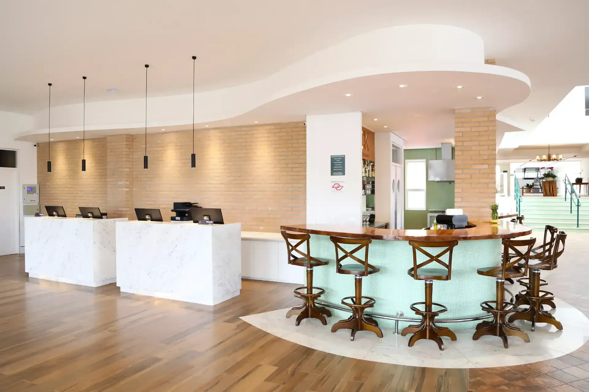 Hall de entrada do hotel com recepção e bar, piso de madeira e paredes brancas.