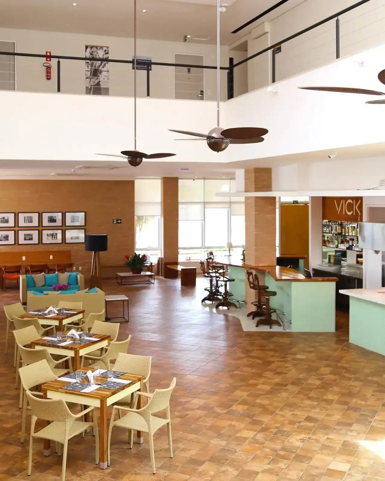 Foto do interior de um restaurante com mesas, cadeiras, área de bar e varanda no segundo andar. Decoração em tons terrosos.