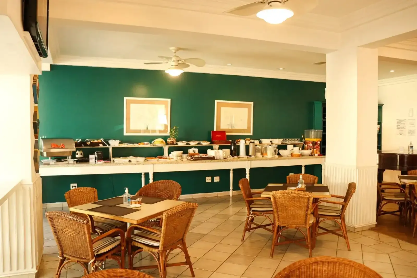 Buffet de café da manhã em uma sala de jantar com cadeiras de vime e uma parede com detalhes em azul-petróleo.