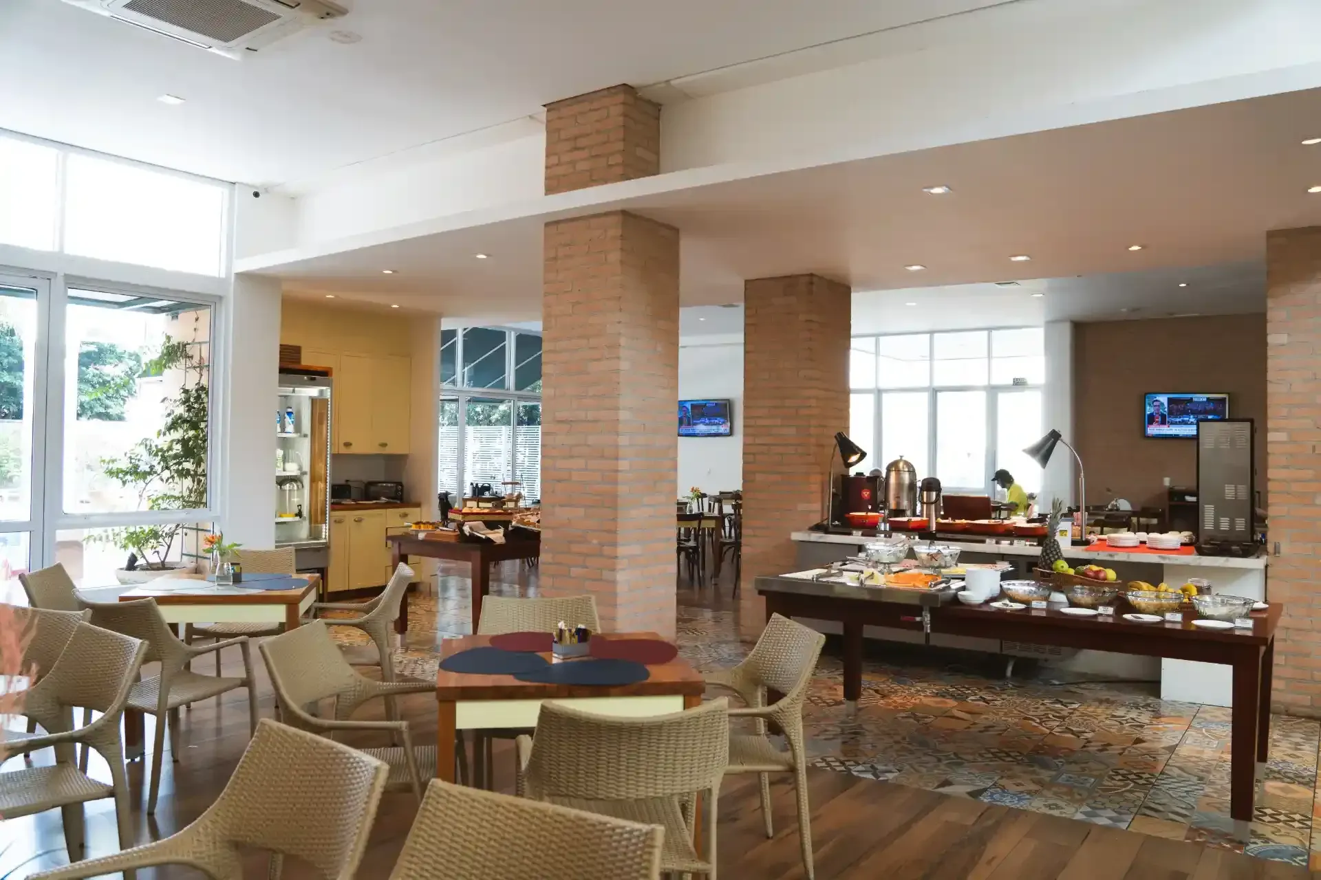 Interior luminoso de restaurante com mesas, buffet e colunas de tijolos.