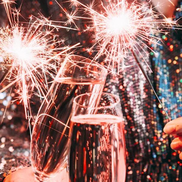 Taças de champanhe cintilantes com velas de faísca acesas contra um fundo de lantejoulas.