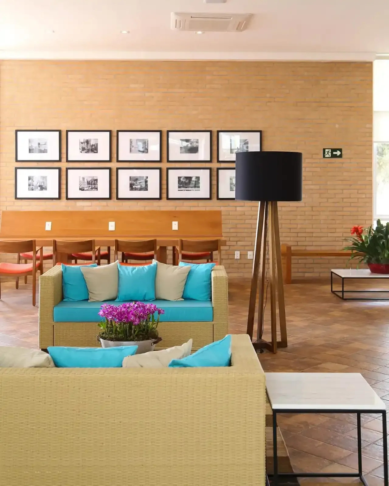 Uma área de espera bem iluminada com dois sofás, uma parede de tijolos com fotos emolduradas e um abajur de chão.