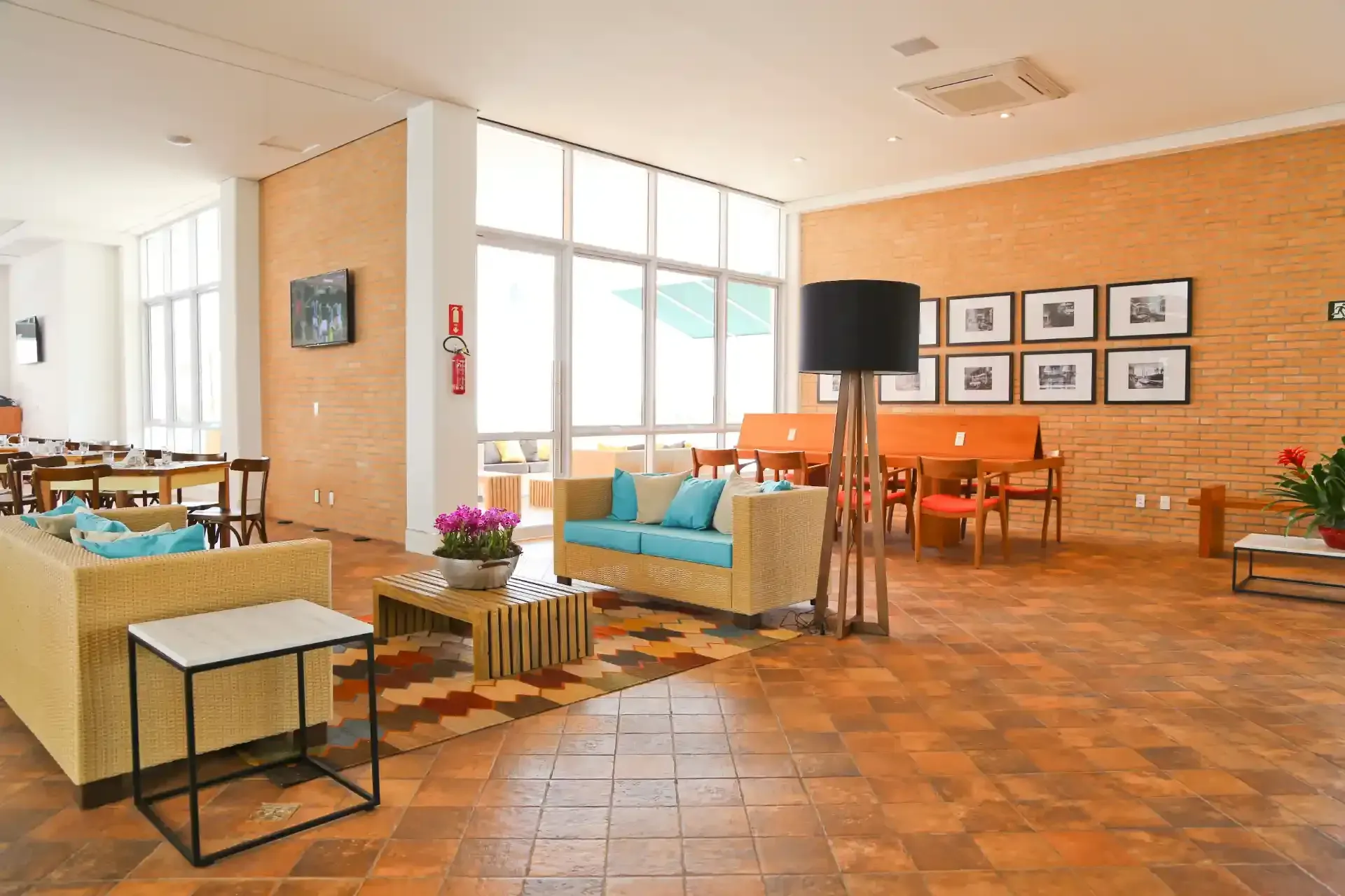 Um saguão bem iluminado com paredes de tijolos, móveis de vime e grandes janelas.