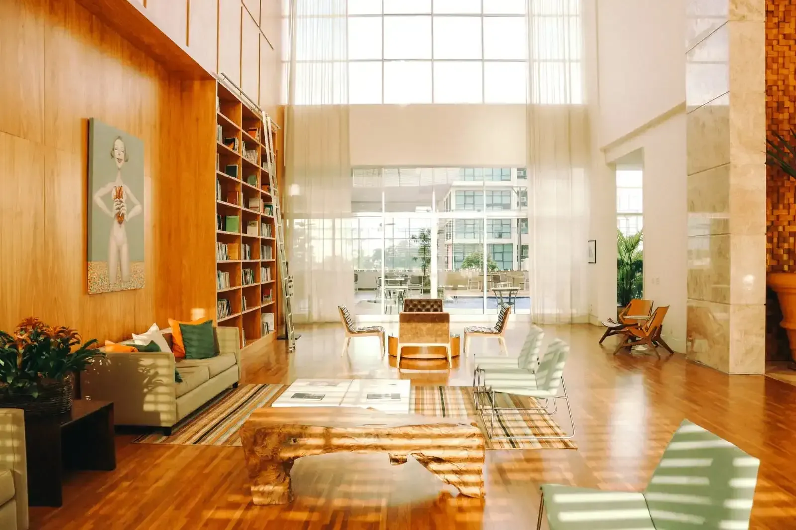 Hall de entrada elegante com painéis de madeira, áreas de estar, janelas amplas e estantes de livros.