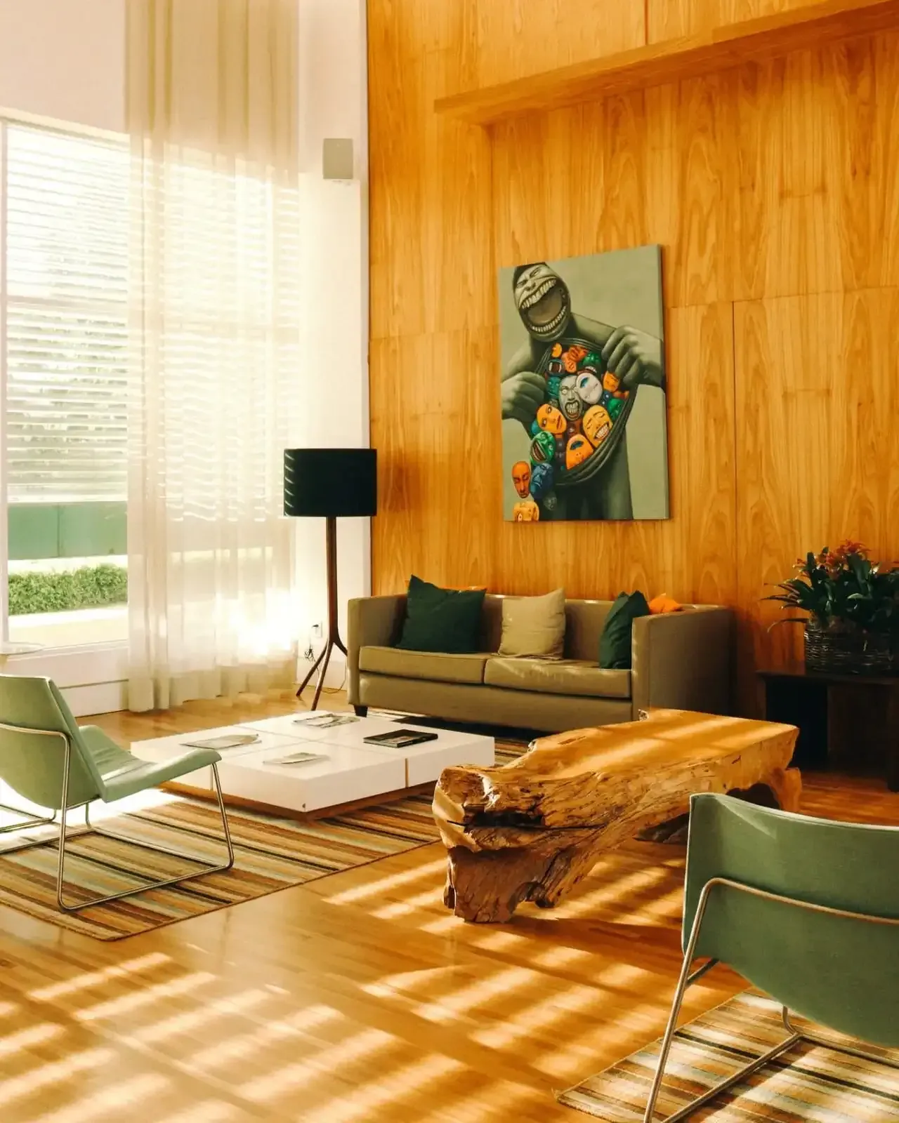 Sala de estar com painéis de madeira, obras de arte, cadeiras verdes e uma longa mesa de centro de madeira.