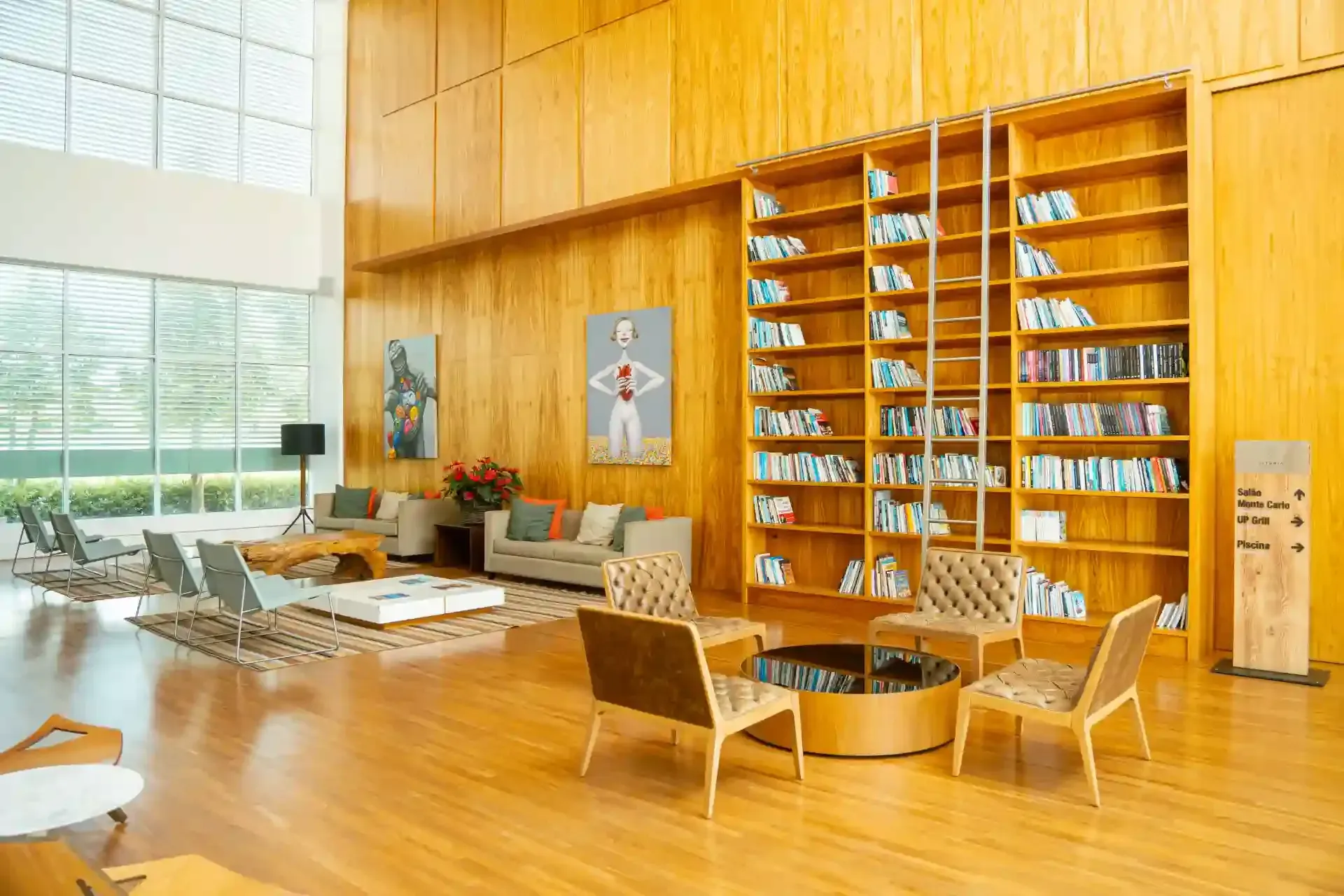Interior de biblioteca com painéis de madeira, estantes de livros, assentos e obras de arte.