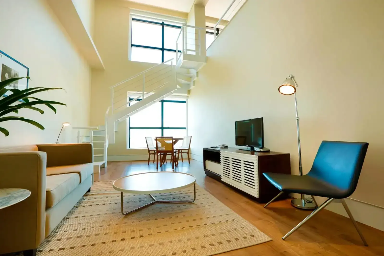 Sala de estar com pé-direito alto, escada em espiral, sofá, TV e mesa de jantar.