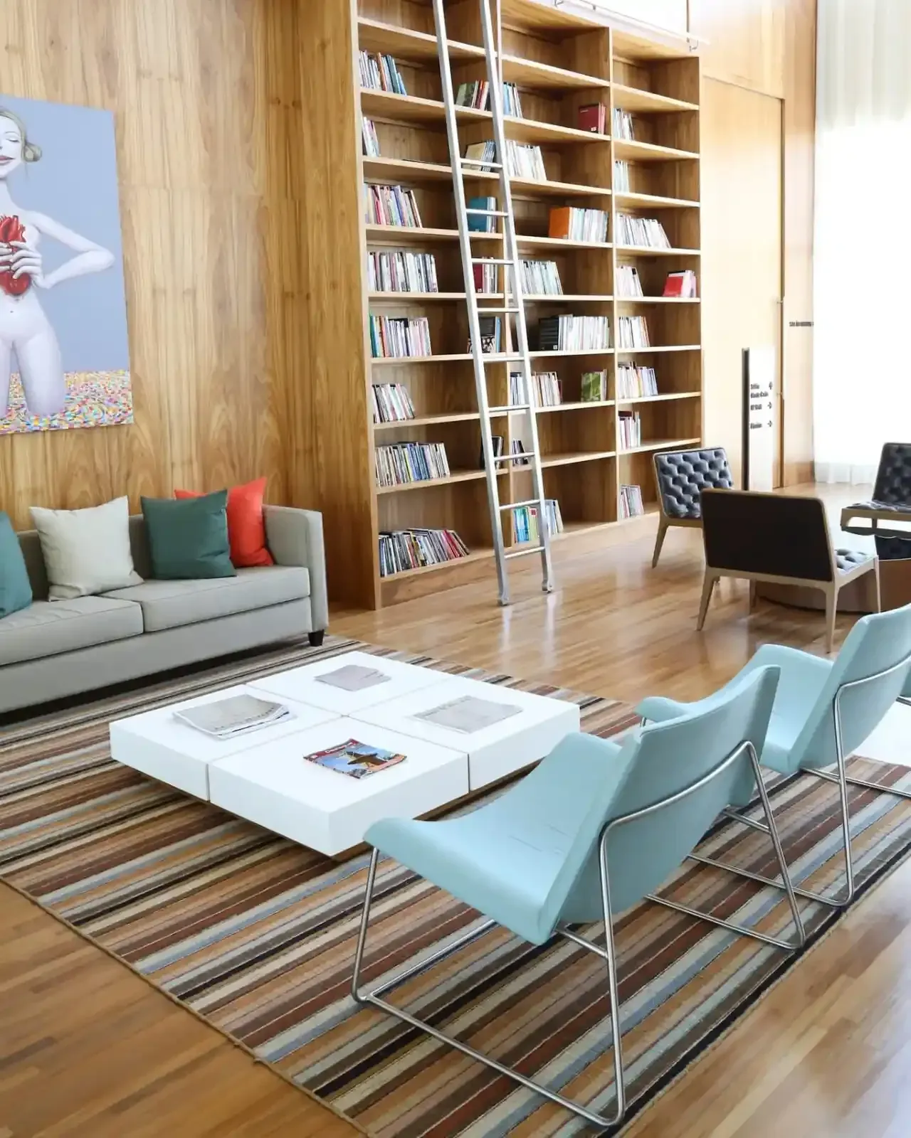Biblioteca com estantes de madeira, escada, assentos e obras de arte. Um espaço moderno e convidativo.