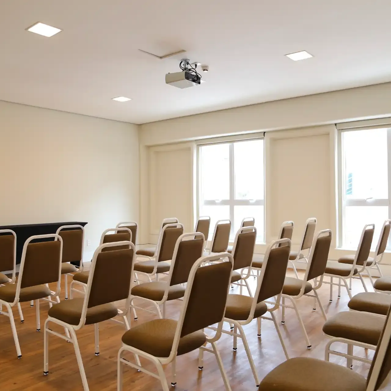 Público em sala de conferências com apresentador no palco, detalhes em verde, duas telas, vista aérea.