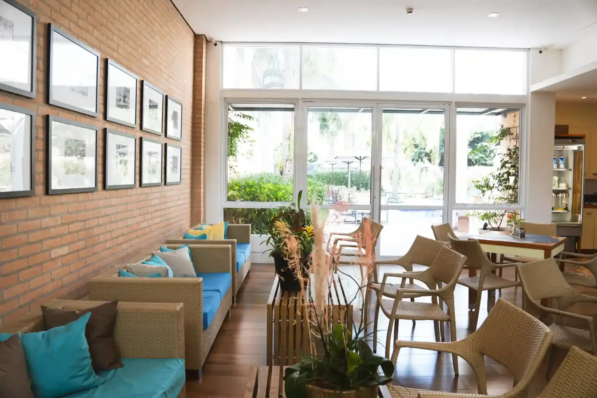 Área de estar com parede de tijolos, obras de arte emolduradas, móveis de vime e portas de vidro que se abrem para uma área de estar externa.