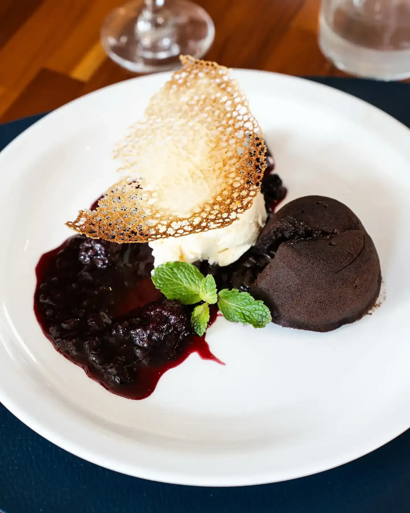 Bolo vulcão de chocolate com sorvete, calda de frutas vermelhas e uma bolacha crocante servido em um prato branco.