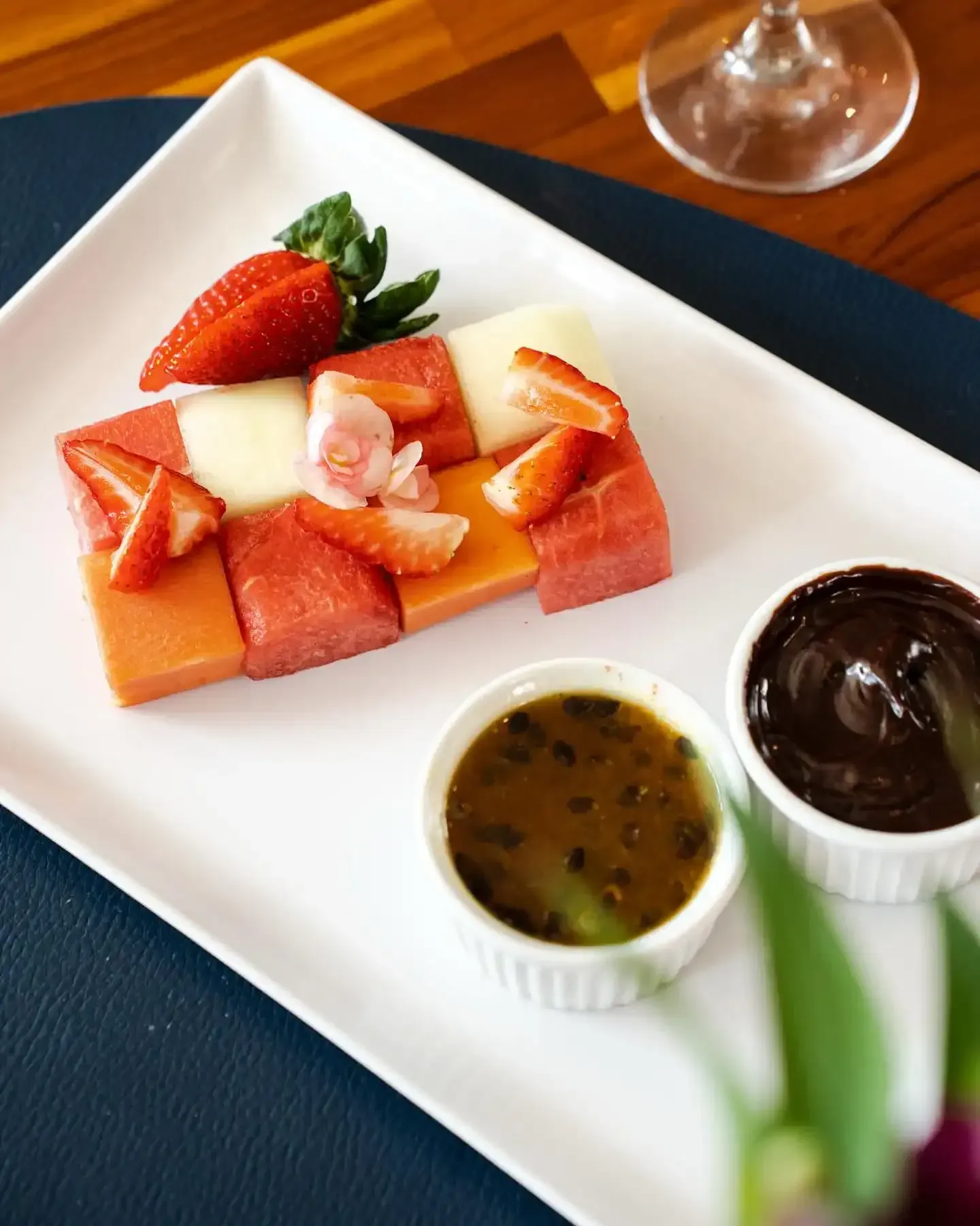 Prato de frutas com melão, mamão e morangos, servido com molhos de chocolate e maracujá.