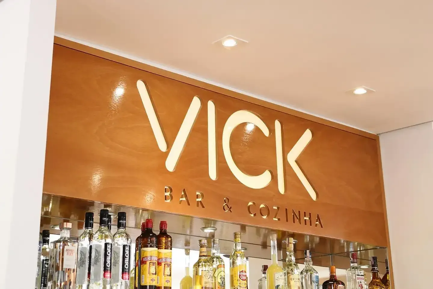 Placa do Vick Bar & Kitchen com garrafas de bebidas alcoólicas no balcão logo abaixo.