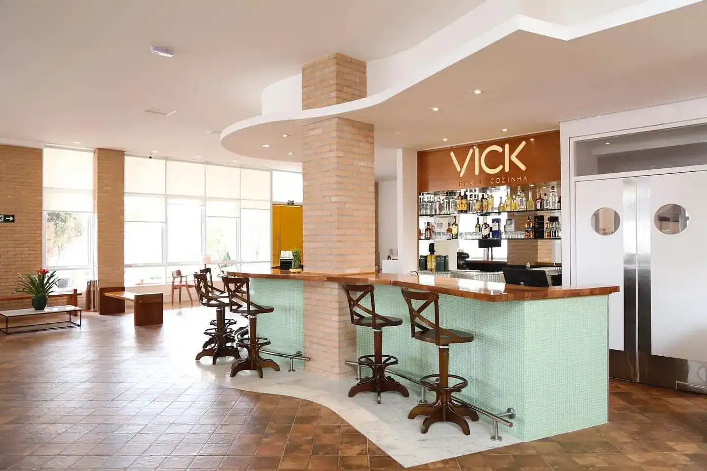 Vista interna de um bar com banquetas, balcão e garrafas de bebidas alcoólicas contra uma parede revestida de madeira, com a placa 