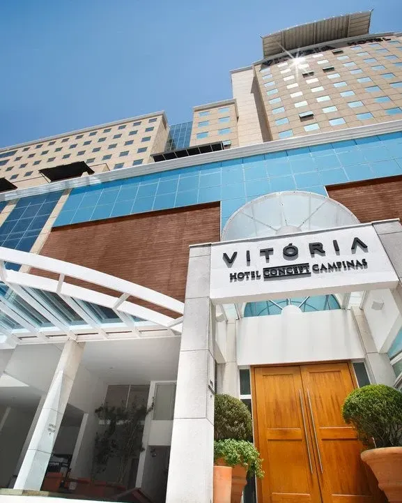 O Hotel Vitória é um edifício alto com fachada de vidro e tijolo e uma entrada coberta por um toldo.