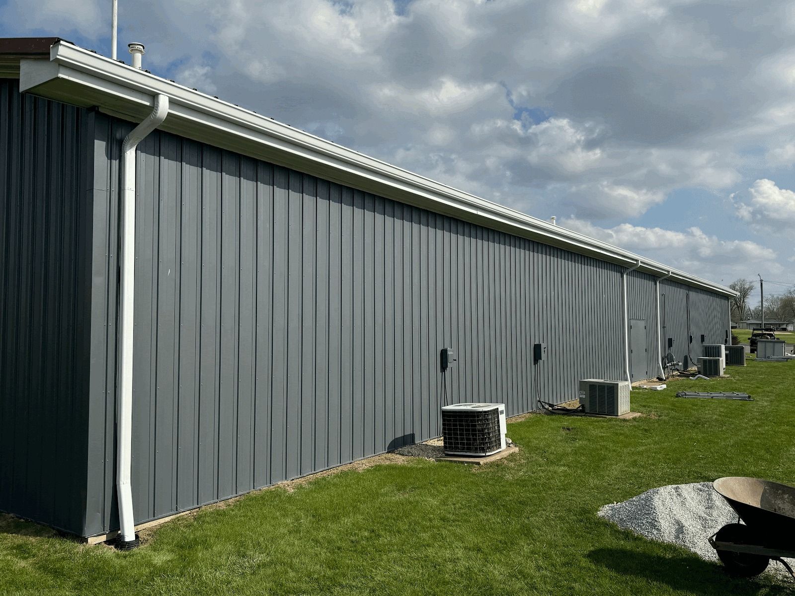 Man in red hat and safety glasses installing black rain gutter on a house.