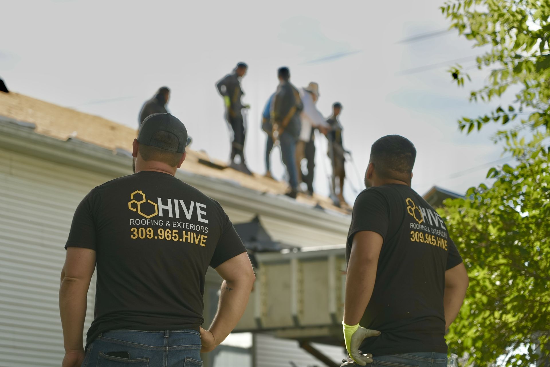 Roofer installs black metal roofing on a house, working near the brick chimney, cloudy sky.