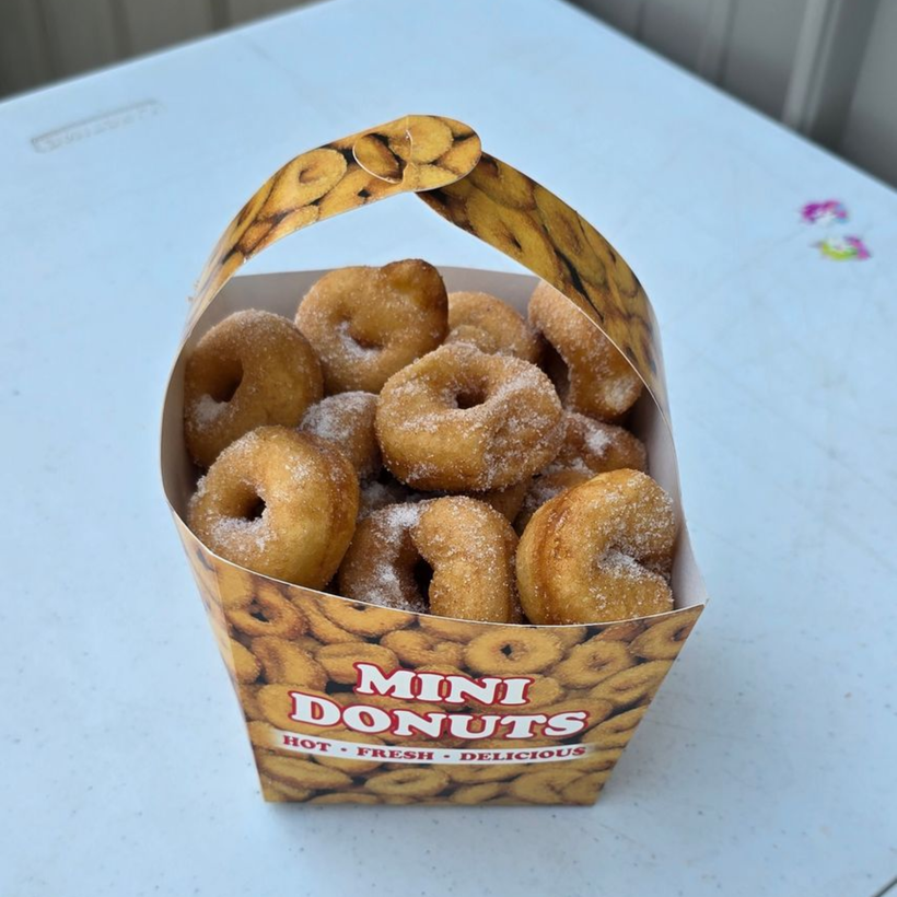Mini donuts with colorful frosting and sprinkles on a wooden board.