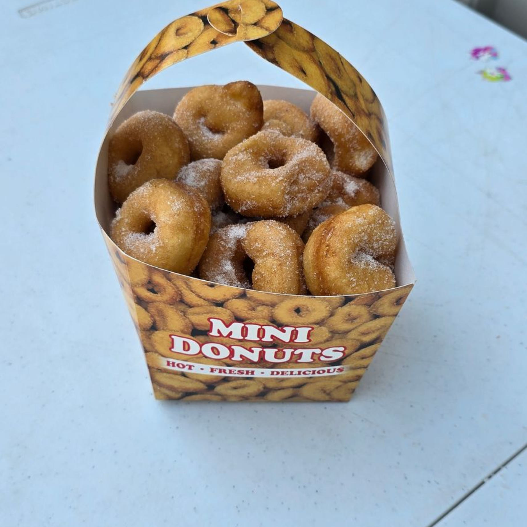 Tray of mini donuts with various frostings and sprinkles on a wooden surface.