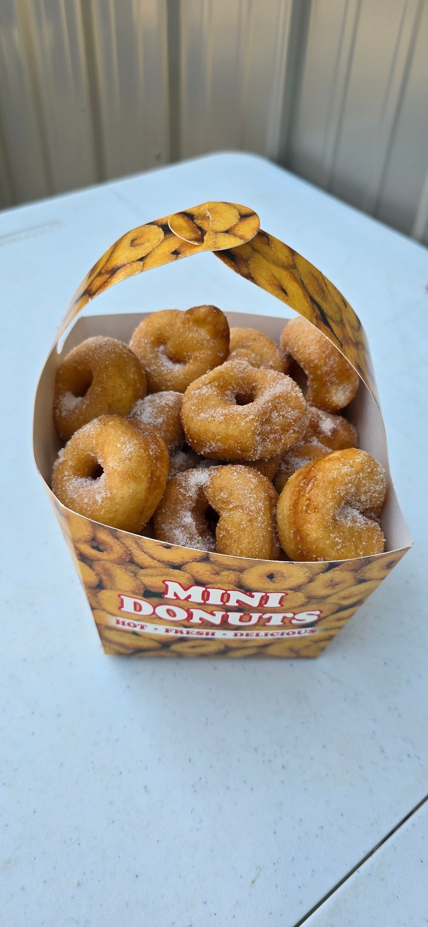 Chocolate-glazed doughnuts with nuts on a wooden board next to a cup of coffee and more doughnuts.