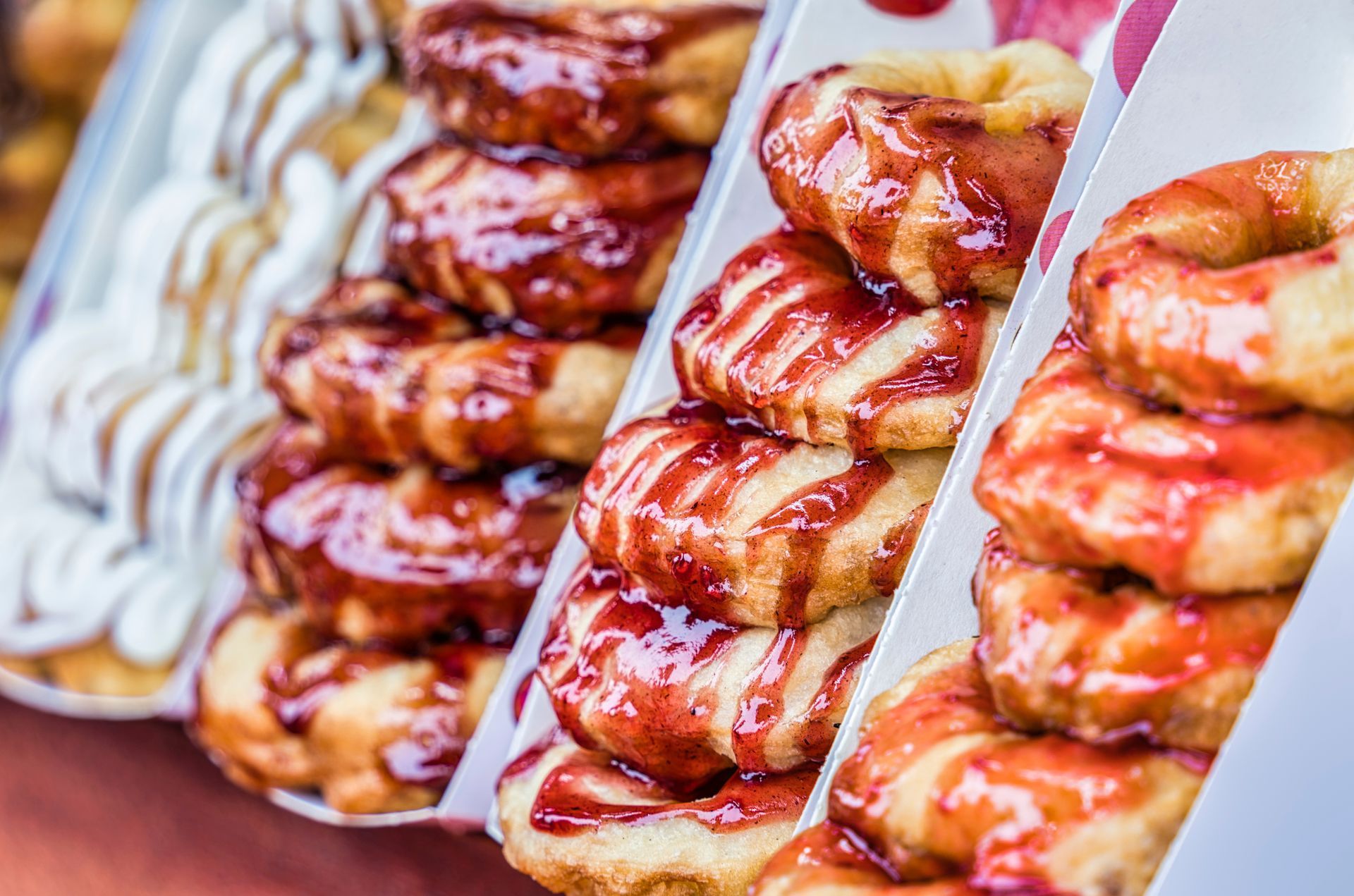 Stacks of glazed donuts in white cardboard boxes; one with white icing, others with red glaze.