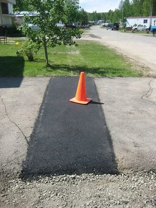 An orange traffic cone is sitting on a patch of asphalt