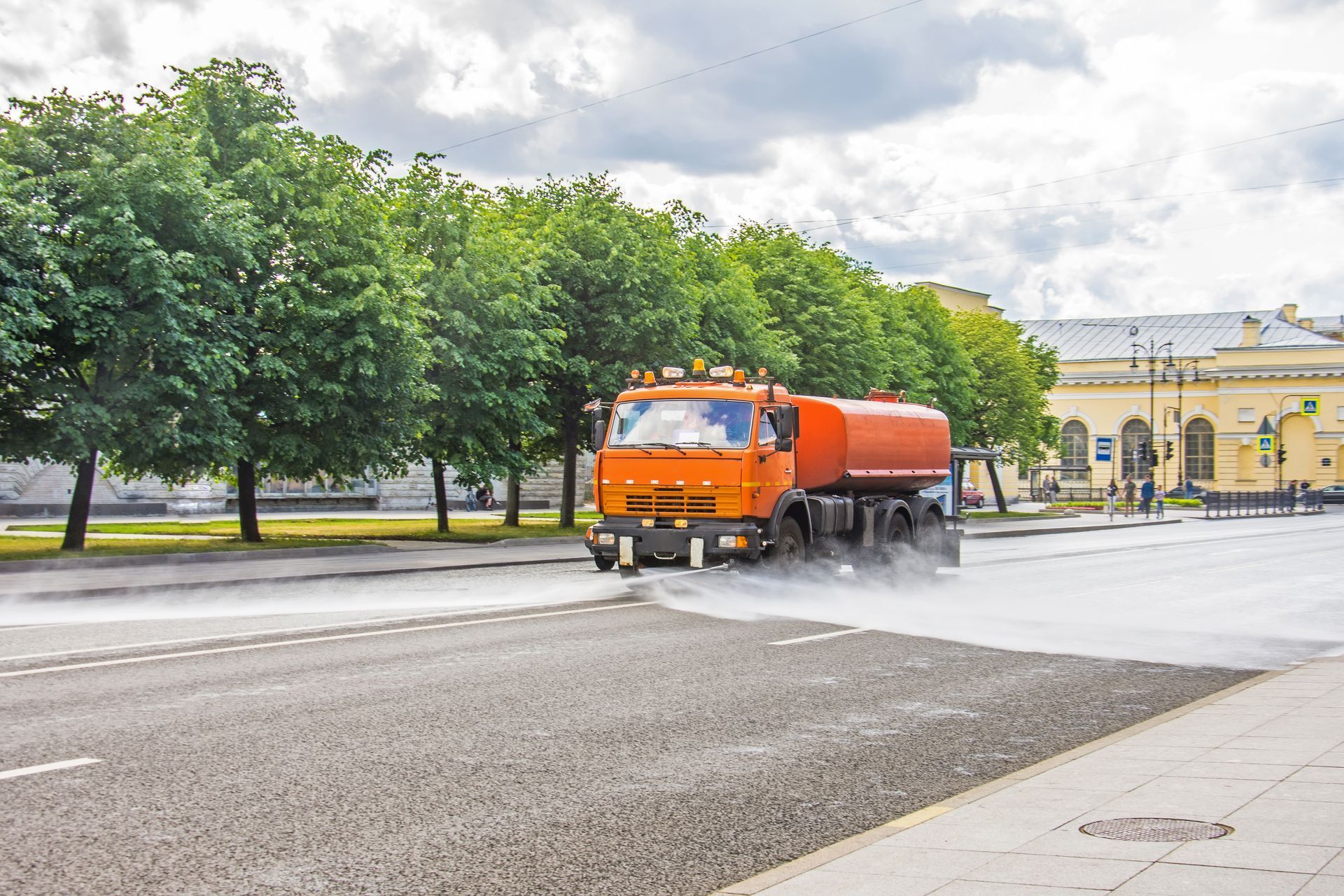 An orange truck is spraying water on a city street.