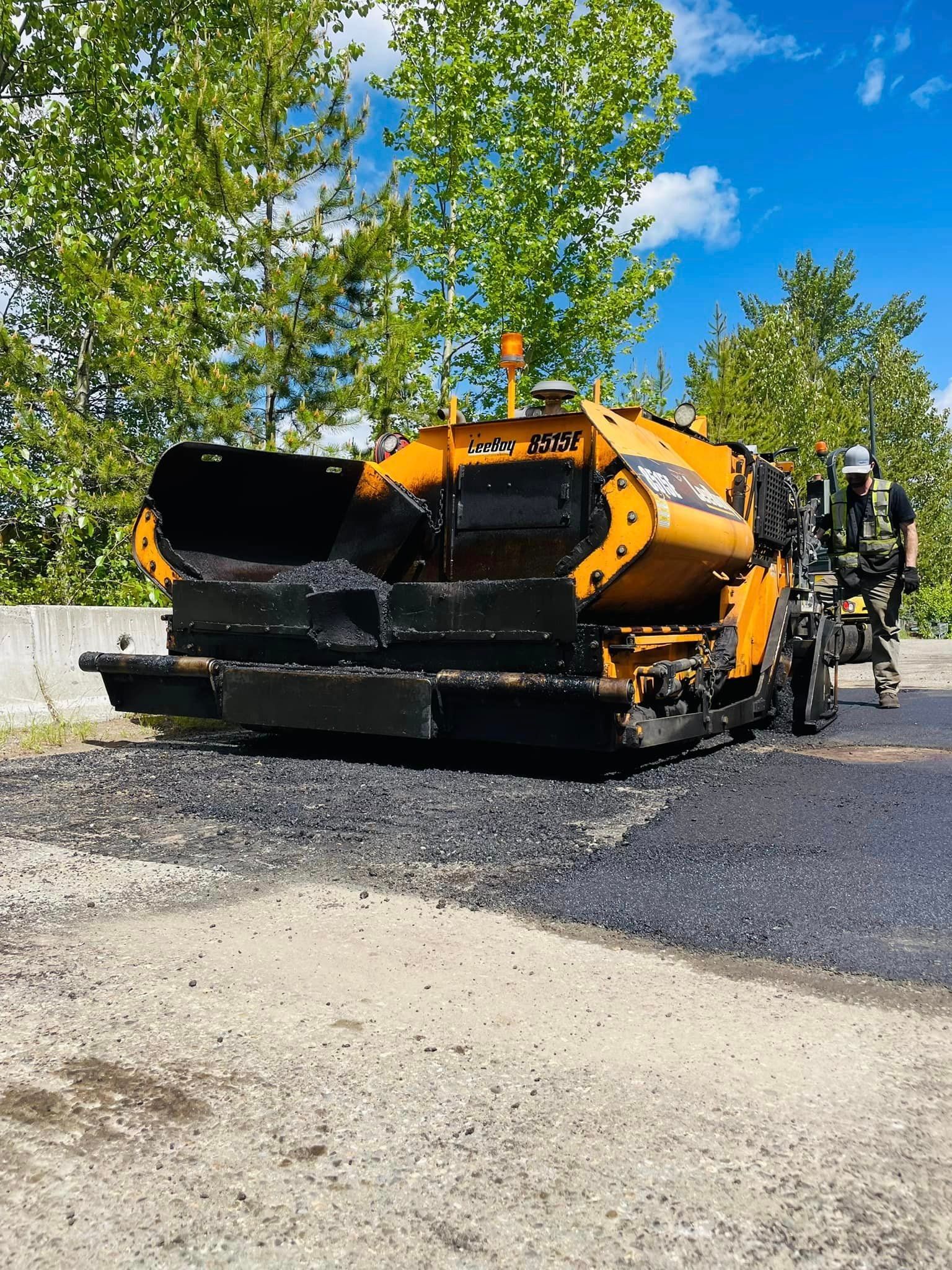 A yellow and black asphalt plow is sitting on the side of a road.