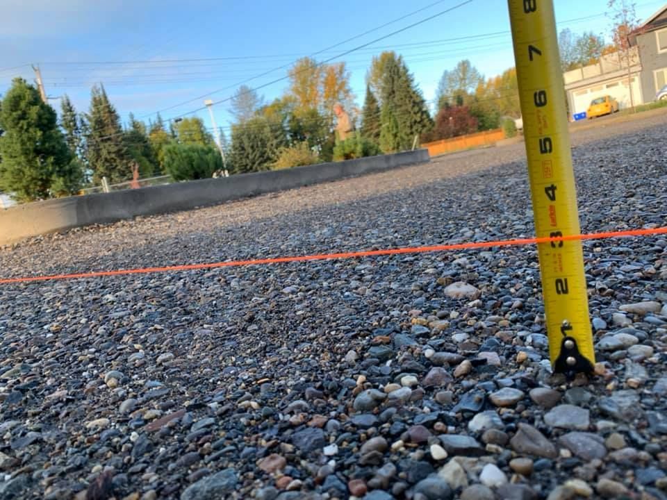 A yellow tape measure is sitting on top of a gravel road.