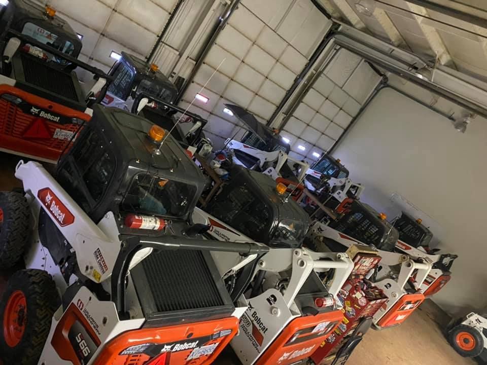 A row of bobcat tractors are lined up in a garage.