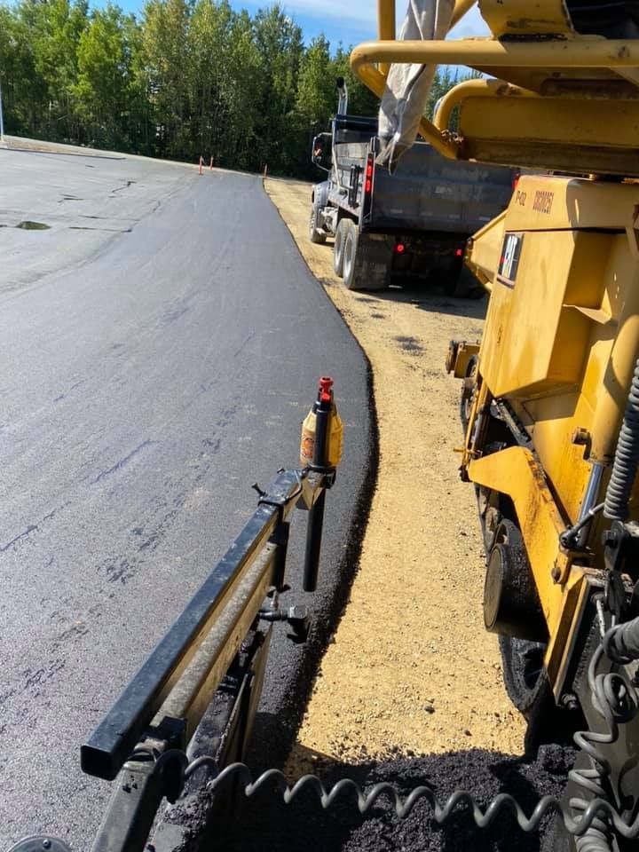 A yellow machine is laying asphalt on the side of a road.