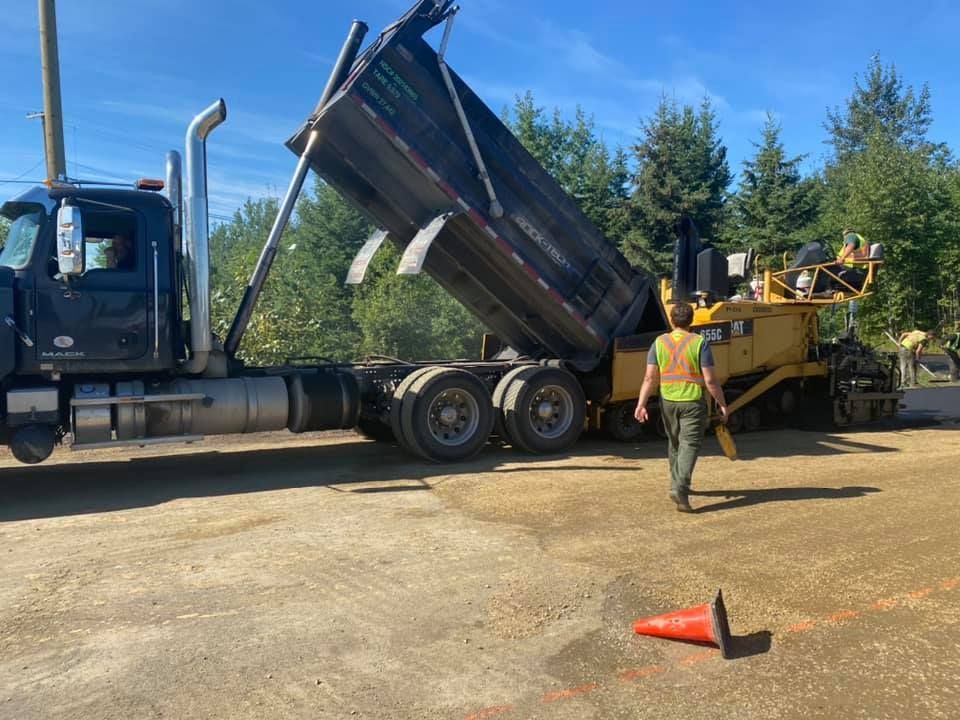 A man is walking in front of a dump truck.