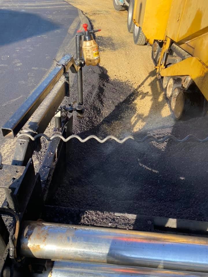 A machine is spreading asphalt on the side of a road.