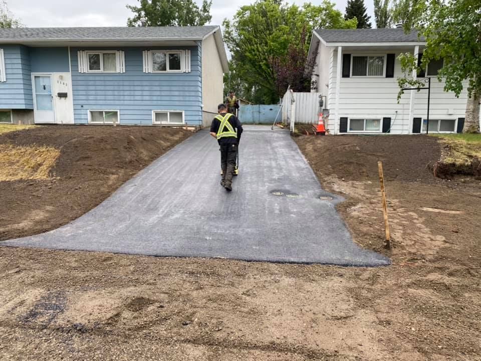 A man is walking down a newly paved driveway in front of a house.
