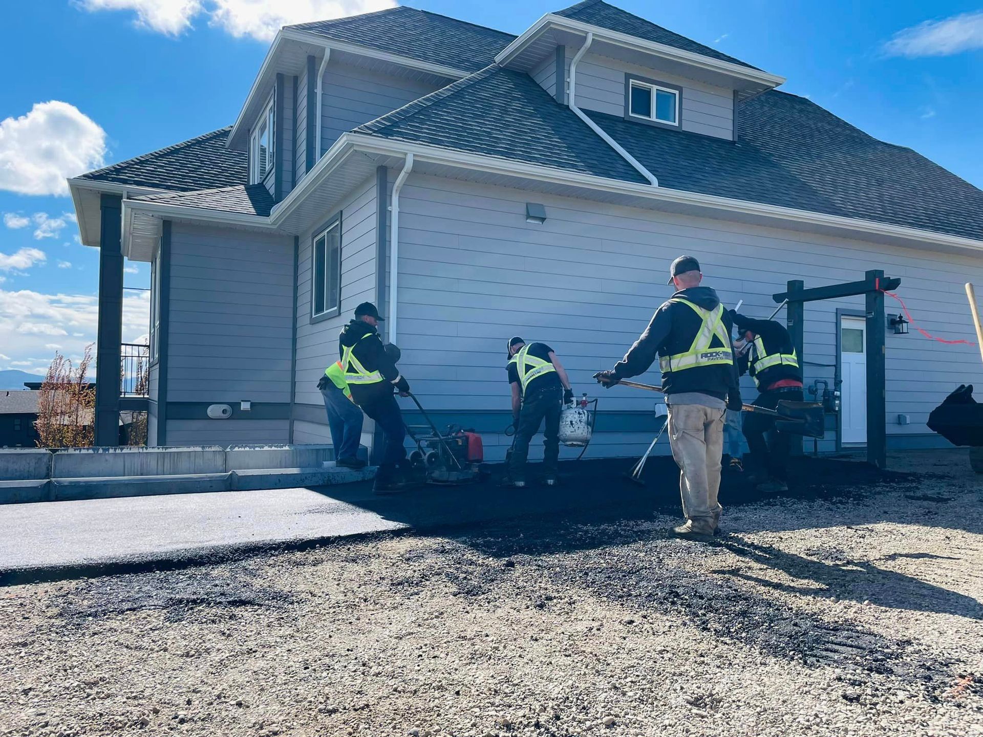 A group of construction workers are working on a driveway in front of a house.