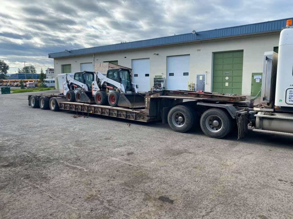 A semi truck is carrying three bobcat skid steers on a trailer.